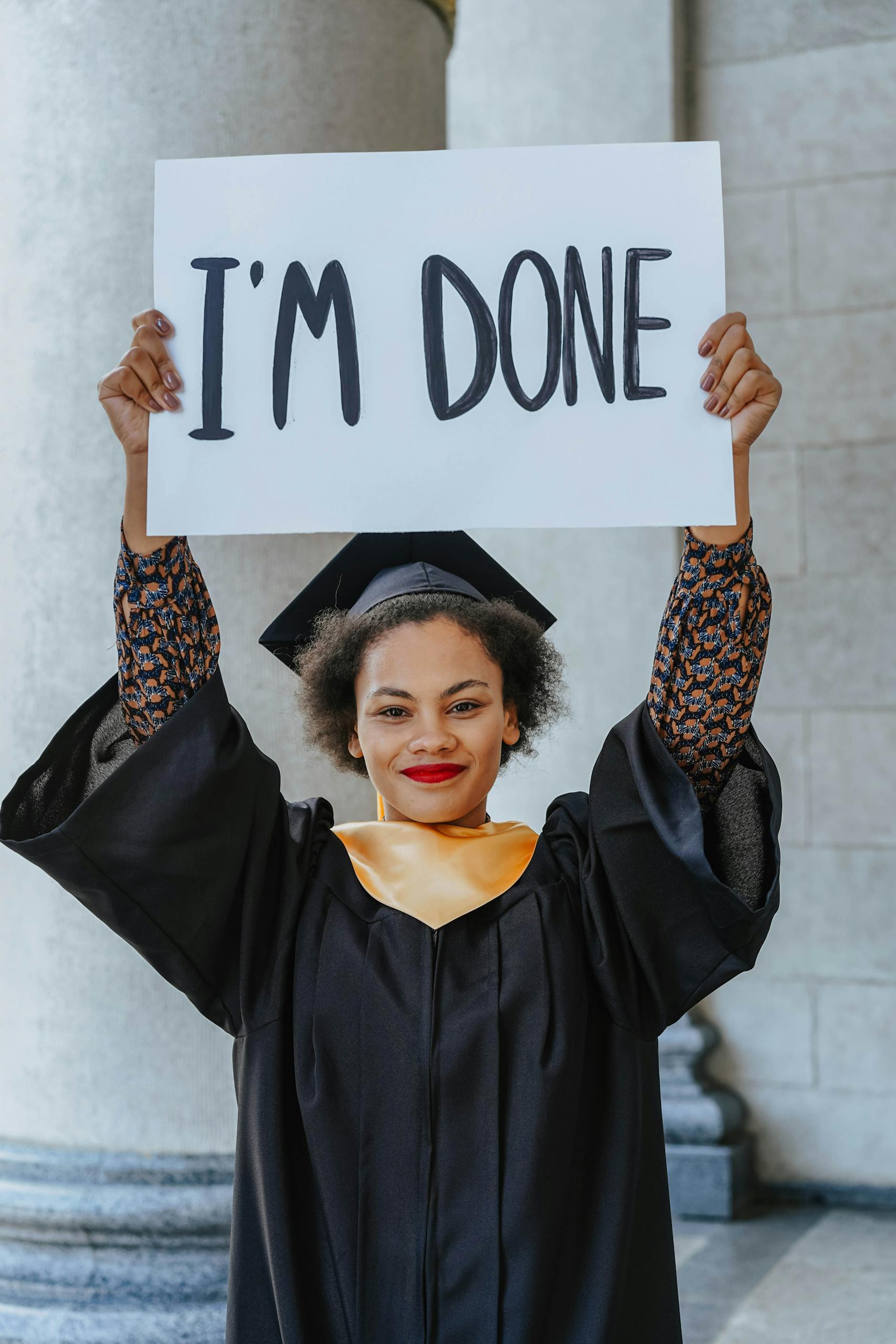 Excited graduate in cap and gown celebrates achievement with an "I'm Done" sign outdoors.